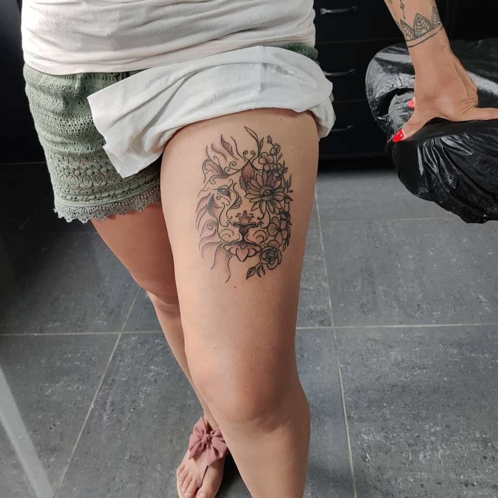 A detailed tattoo on the thigh featuring a lion's face surrounded by floral patterns, blending nature with a bold, artistic design