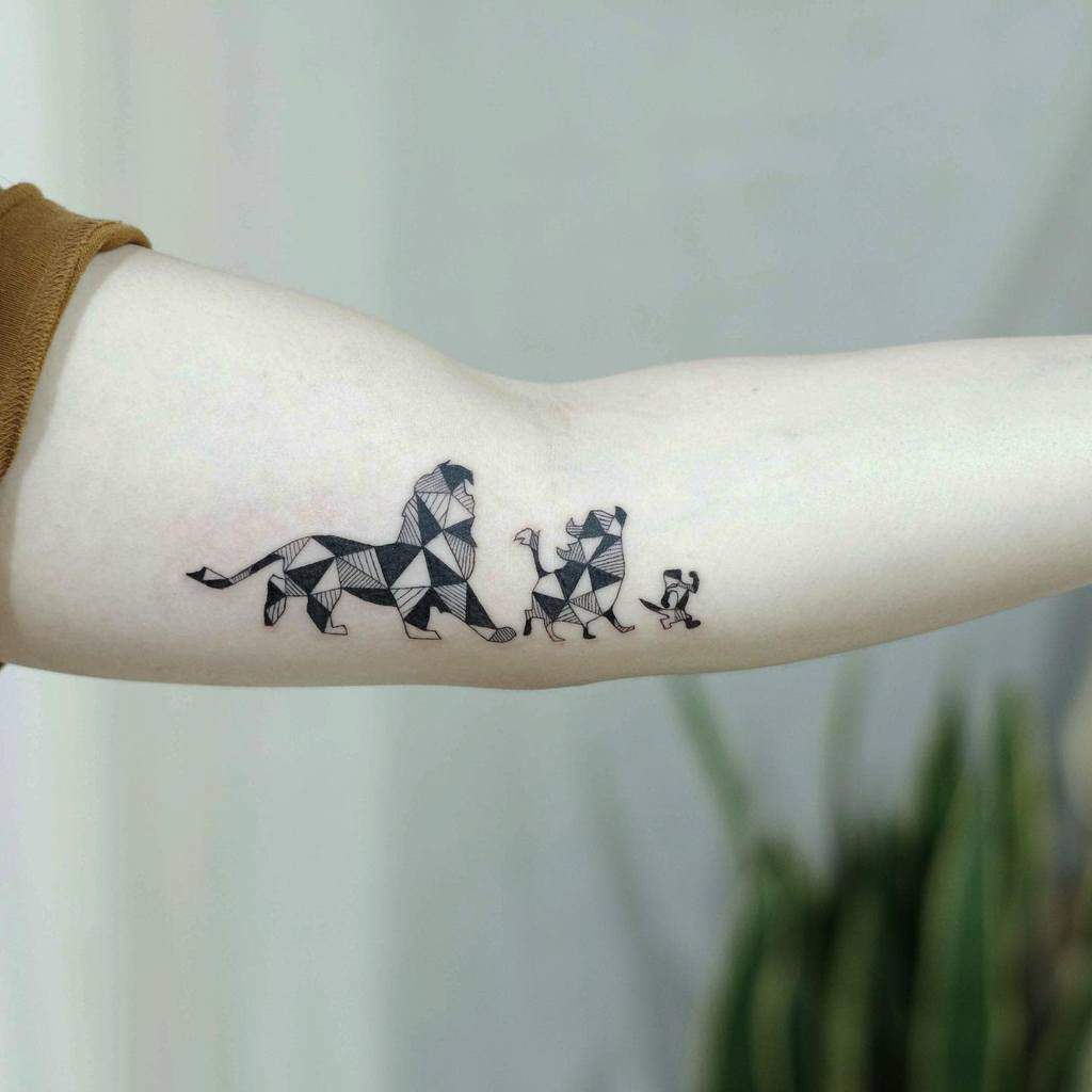 A geometric-style tattoo depicting the iconic characters from The Lion King—Mufasa, Timon, Pumbaa, and Simba—walking together on the forearm