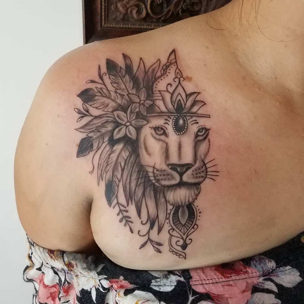 Lion tattoo with floral and decorative elements on a woman's shoulder
