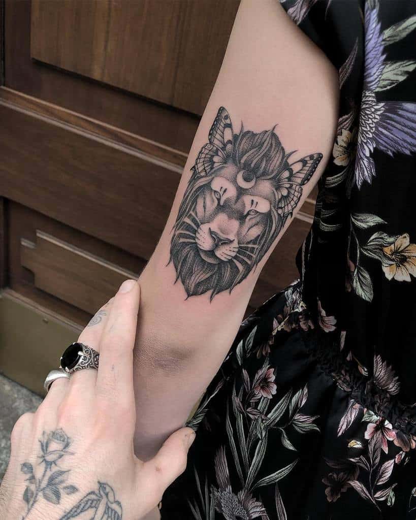 A lion tattoo with a moth and crescent moon on an upper arm