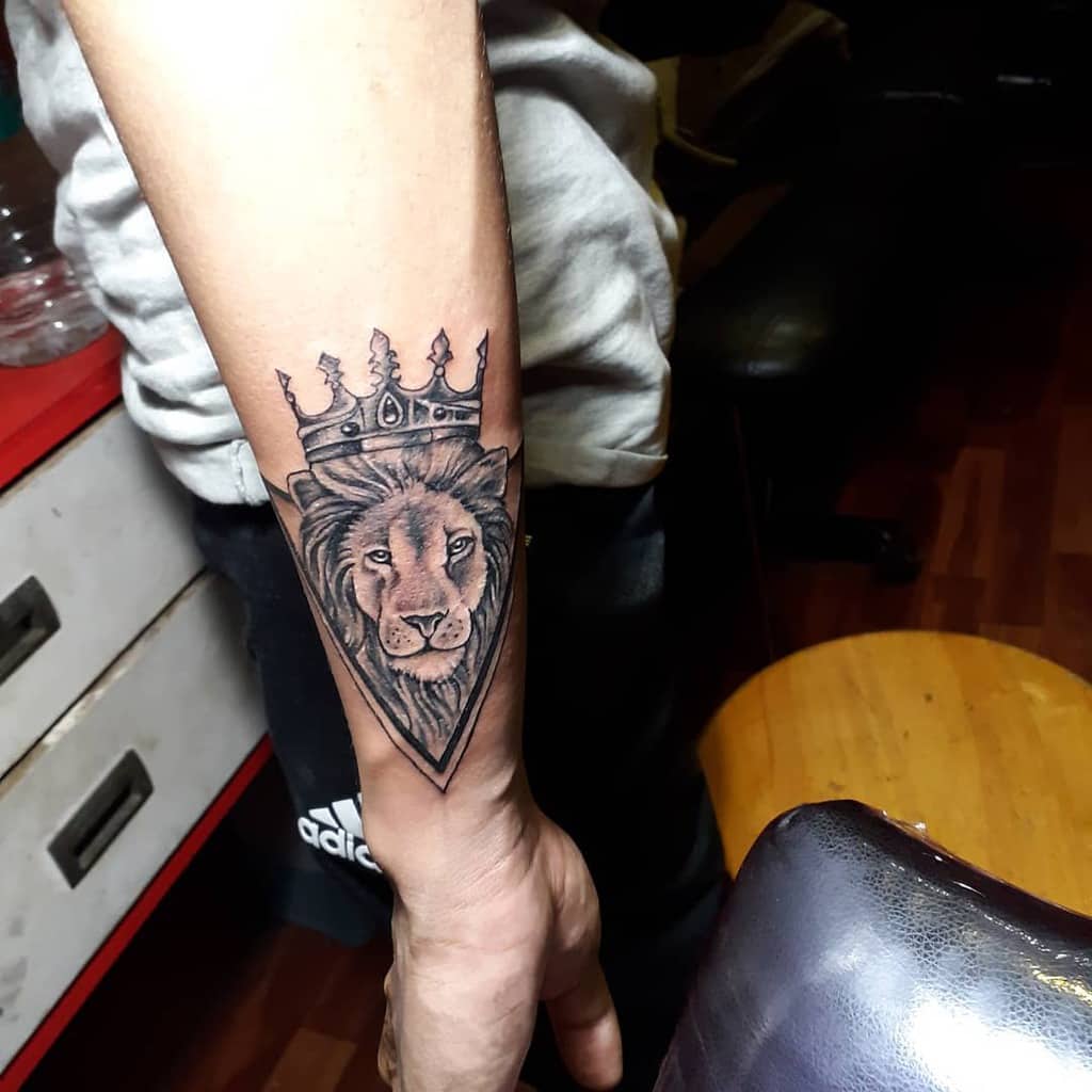 Wrist tattoo of a lion with a crown, shaded in black and gray