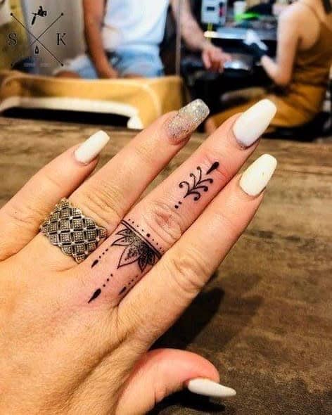 Intricate mandala-inspired finger tattoo with floral patterns and dot details, paired with white and glittery nails for a chic look