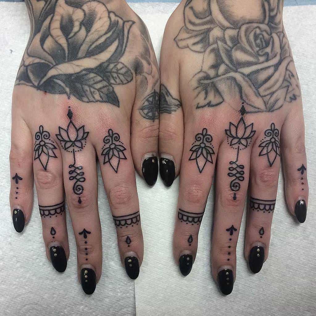 Ornamental finger tattoos featuring lotus designs, symmetrical patterns, and dot accents, paired with bold black nail polish