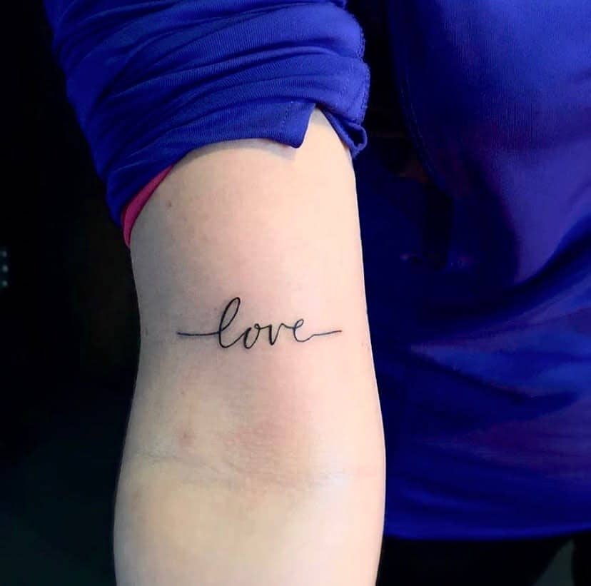 Tattoo of the word "love" in cursive script on a person's arm