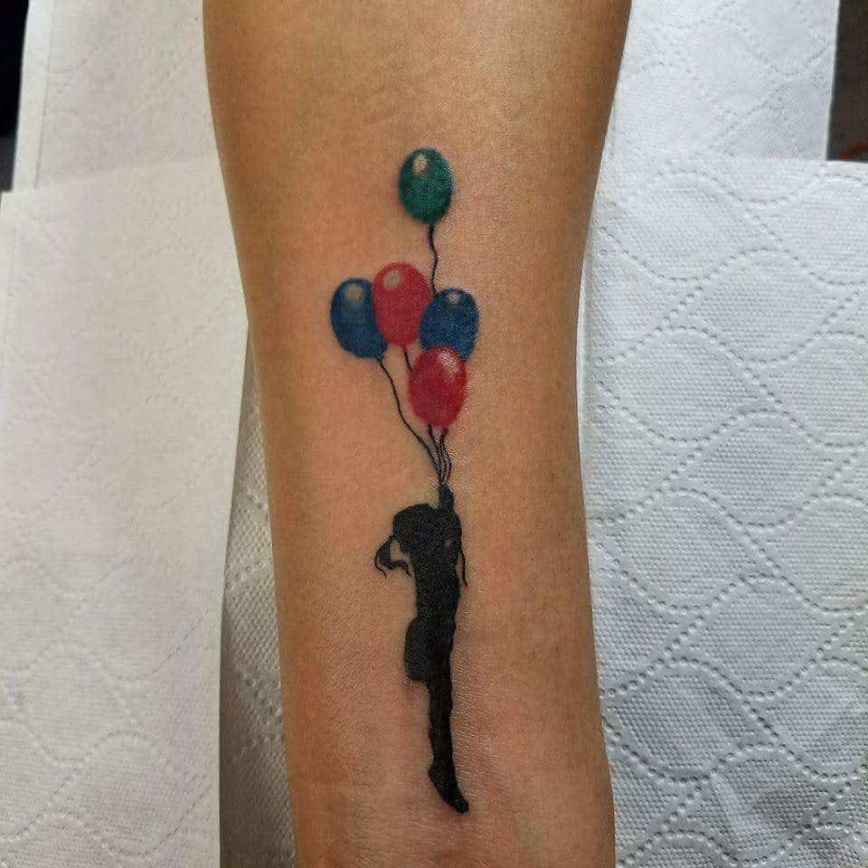 Tattoo of a silhouette holding colorful balloons on a forearm