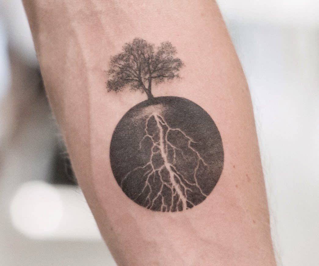 Tattoo of a tree on an arm, with roots extending into a shaded circle