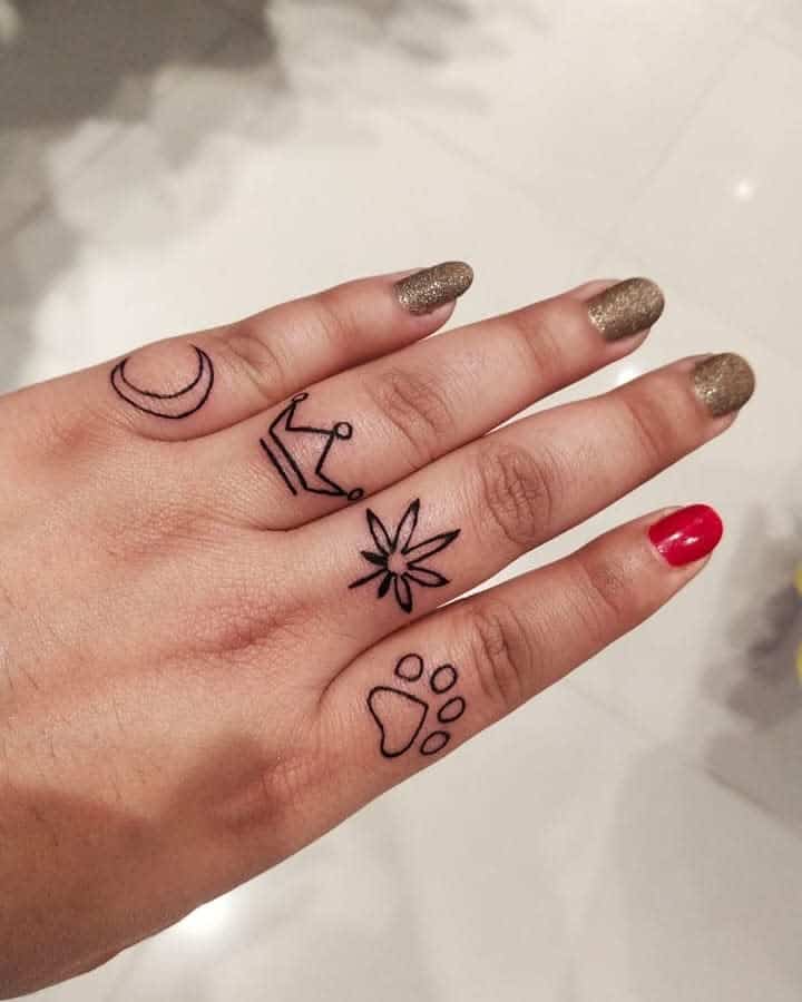 Hand with black line tattoos: crescent moon, crown, leaf, and paw print on fingers