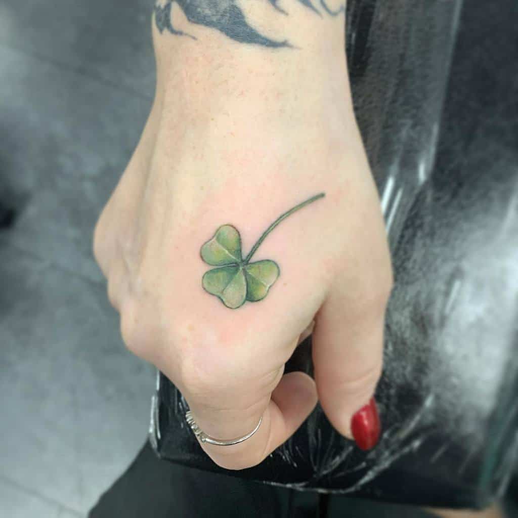 A hand with a small green four-leaf clover tattoo near the wrist