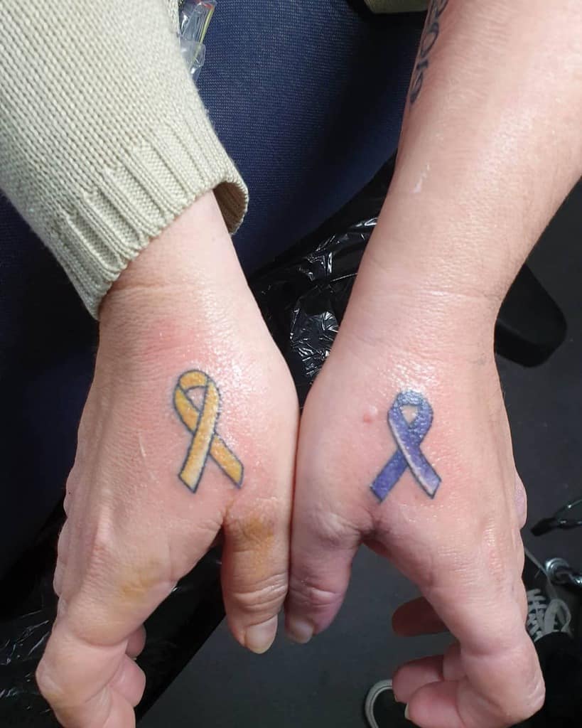 Two hands with yellow and purple ribbon tattoos on the backs