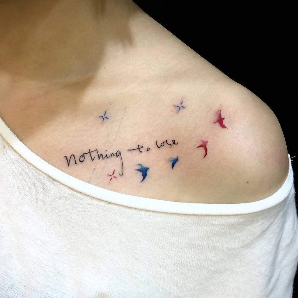 A tattoo on a shoulder with the text "Nothing to lose," surrounded by small colorful stars and birds