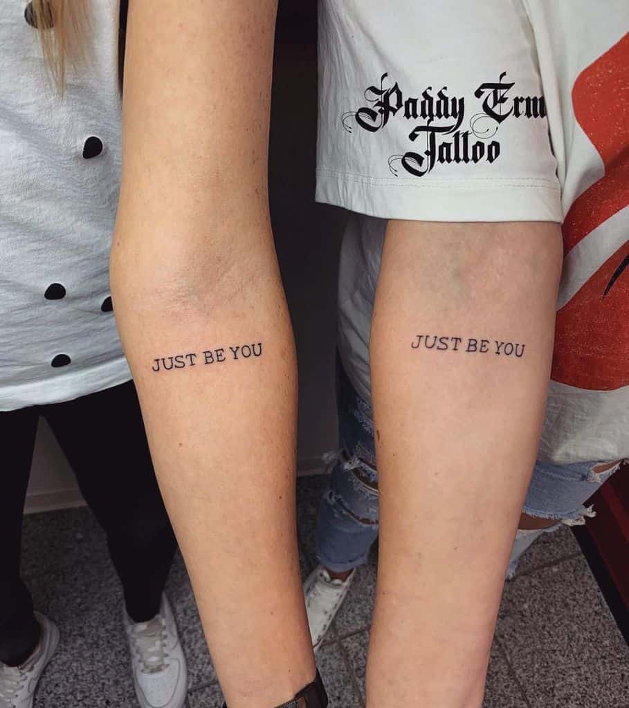 Two people displaying matching "JUST BE YOU" tattoos on their forearms