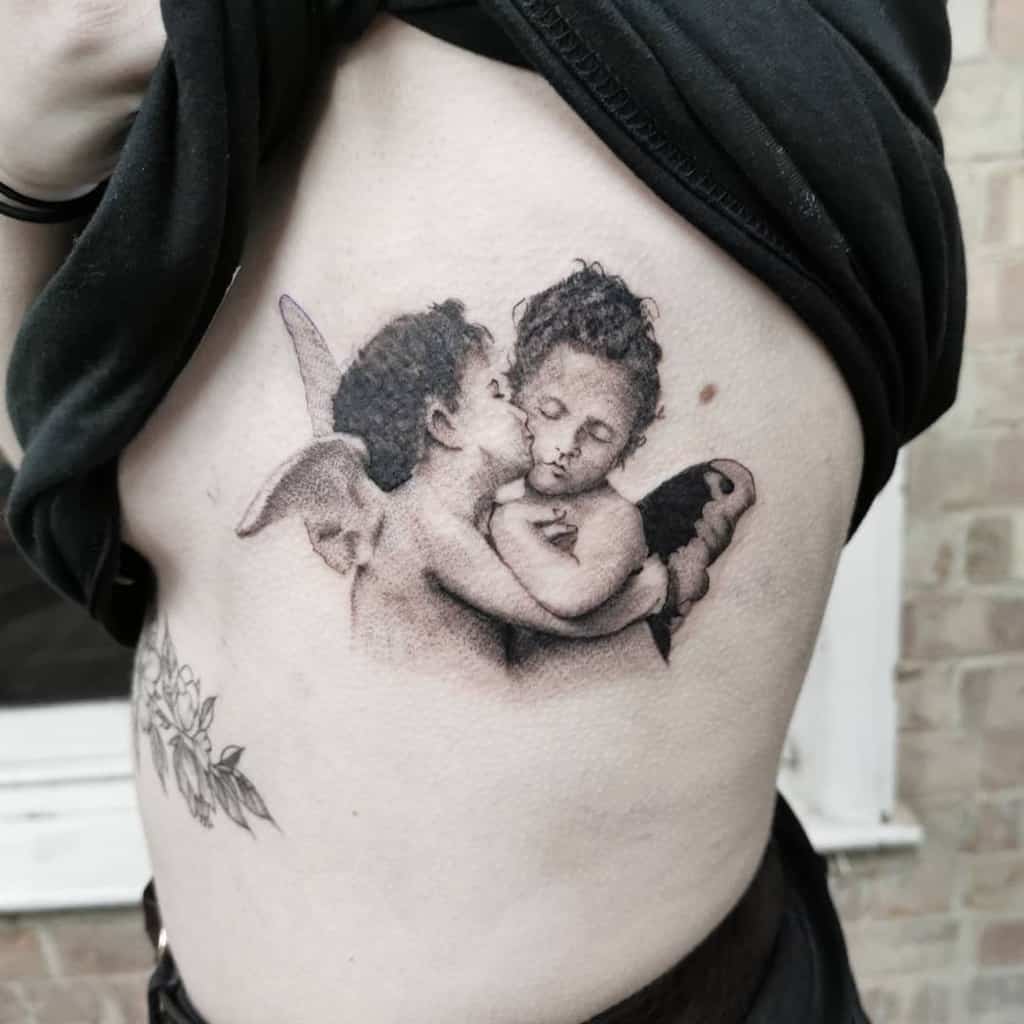 Tattoo of two cherubs kissing, one with wings, on a person's side