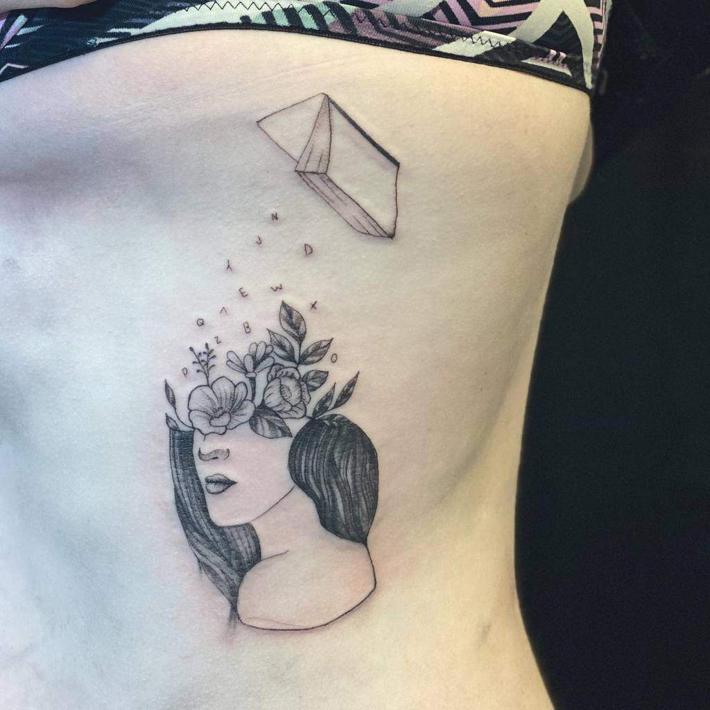 Rib tattoo of a woman with flowers and leaves blooming from her head, accompanied by floating letters and a paper plane