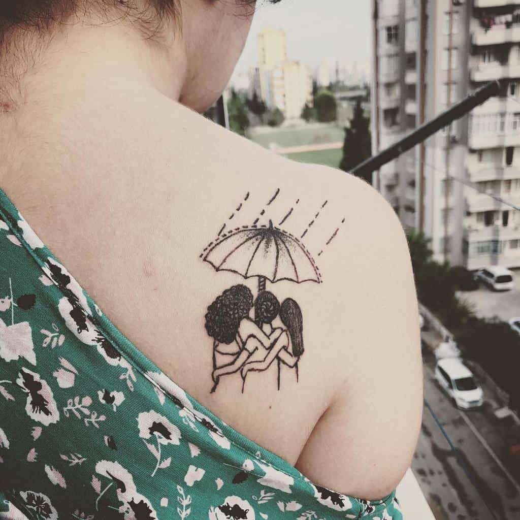 A person with a shoulder tattoo of three people huddled under an umbrella