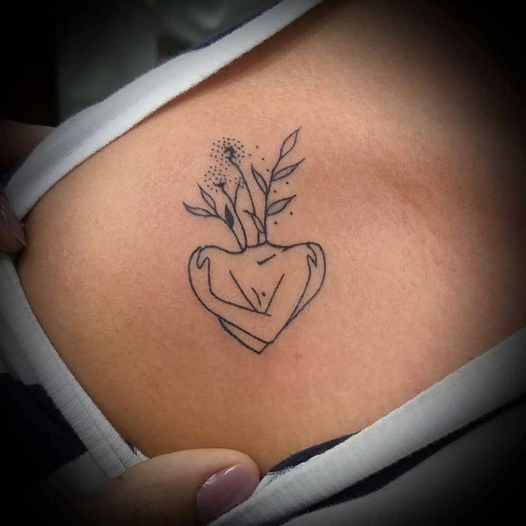 Delicate shoulder tattoo of a heart-shaped vase with flowers and leaves sprouting from it, in minimalist line art