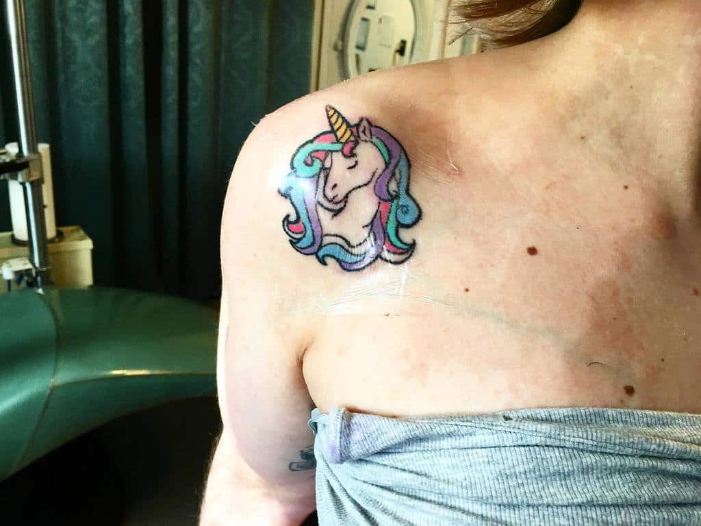 A person with a colorful unicorn tattoo on their shoulder