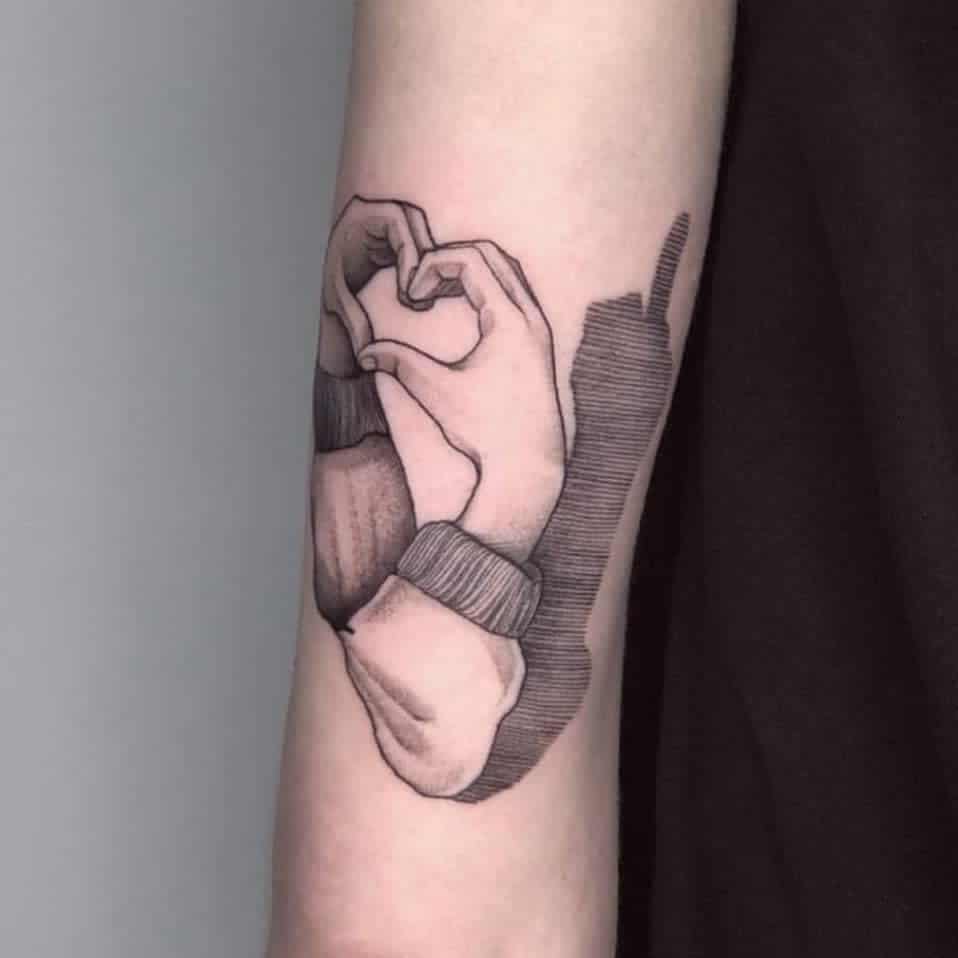 Tattoo of hands forming a heart shape on a forearm
