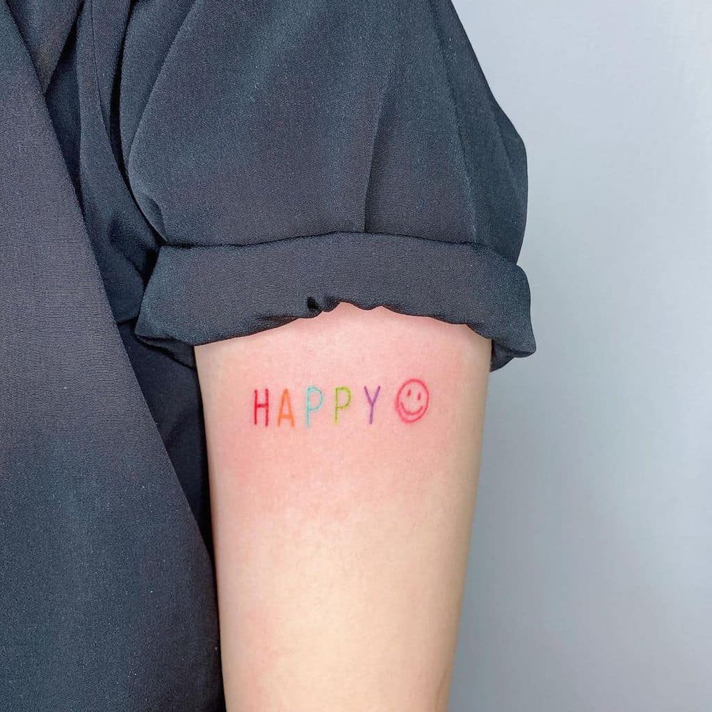 Arm with "HAPPY" in rainbow colors and a smiley face tattoo on the upper arm