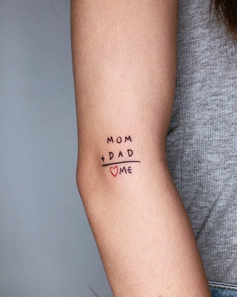 Tattoo on an arm showing "Mom + Dad = Me" with a heart symbol