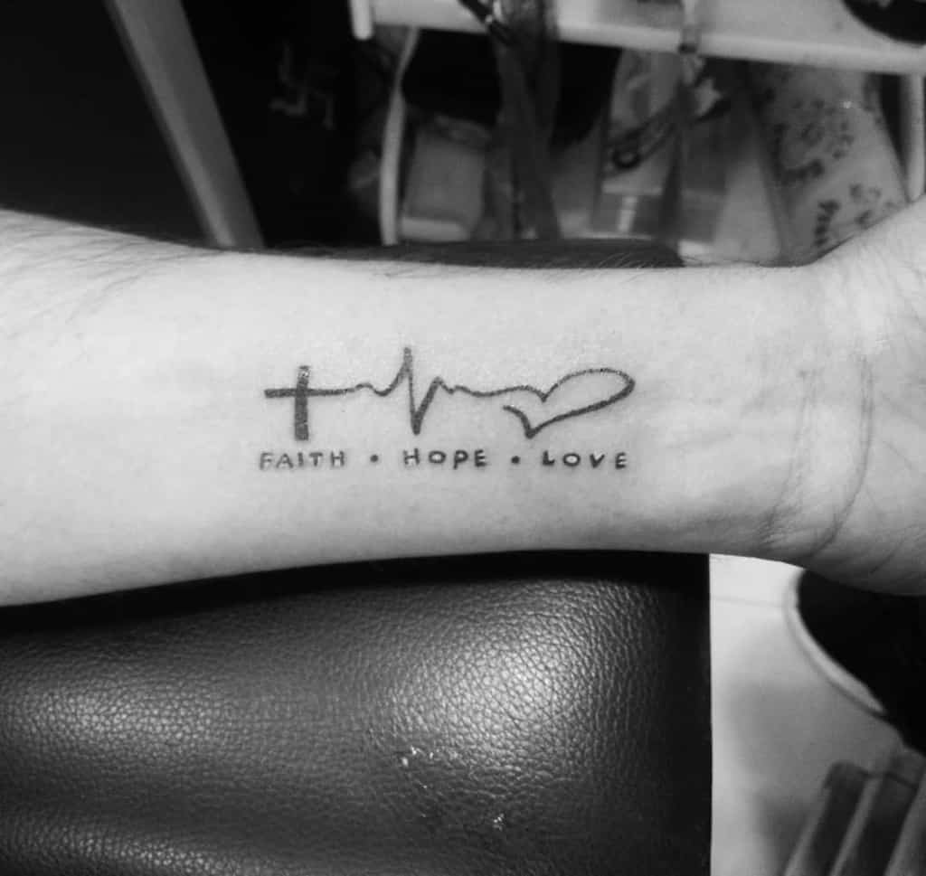 Arm tattoo with a cross, heartbeat line, heart silhouette, and the words "Faith Hope Love"
