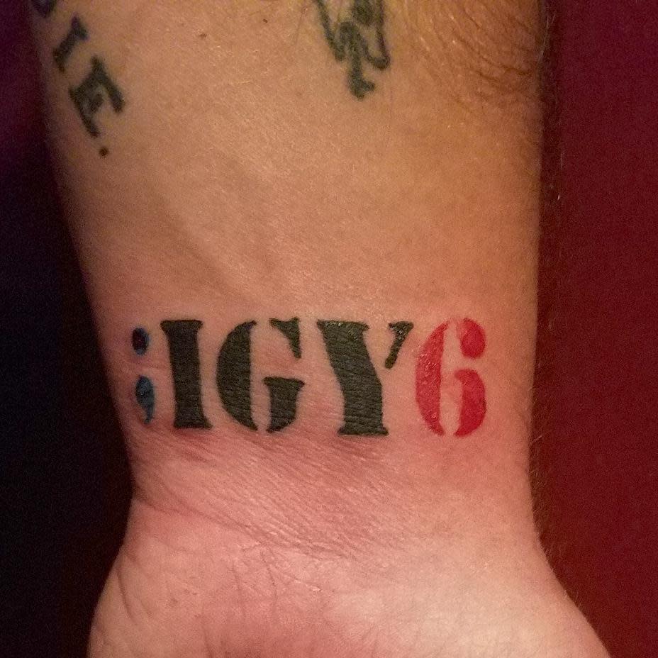Tattoo on a wrist reads ";IGY6" with a semicolon and "6" in red, symbolizing support and awareness
