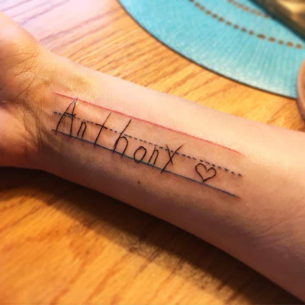Wrist tattoo resembling handwriting, spelling 'Anthony' with a heart at the end, styled like lined notebook paper