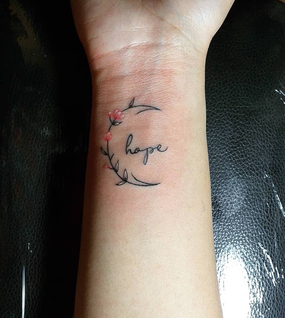 Wrist tattoo with the word "hope" encircled by a delicate floral design with small red flowers