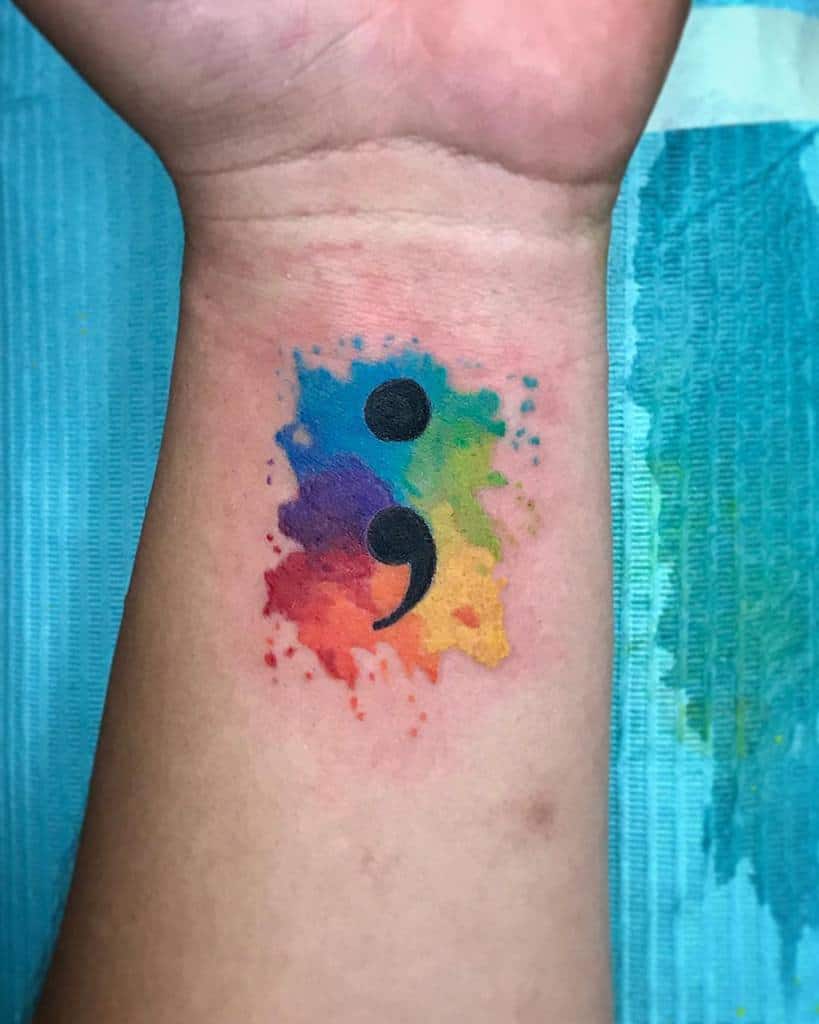 Tattoo of a semicolon over a colorful watercolor splash on a wrist