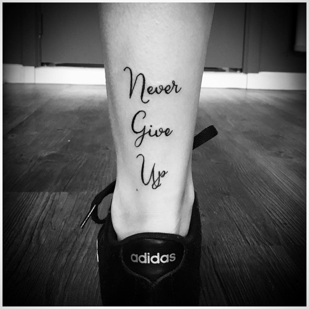 Black and white image of "Never Give Up" tattoo on a person's lower leg 
