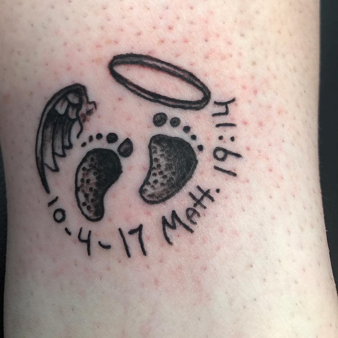 Tattoo of baby footprints, an angel wing, halo, and text "10-4-17, Matt, 1:1" on pale skin