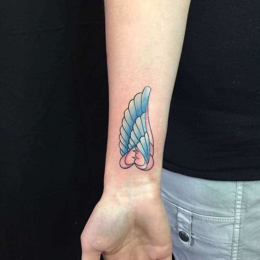Tattoo of an angel wing with shades of blue and pink on the inner forearm