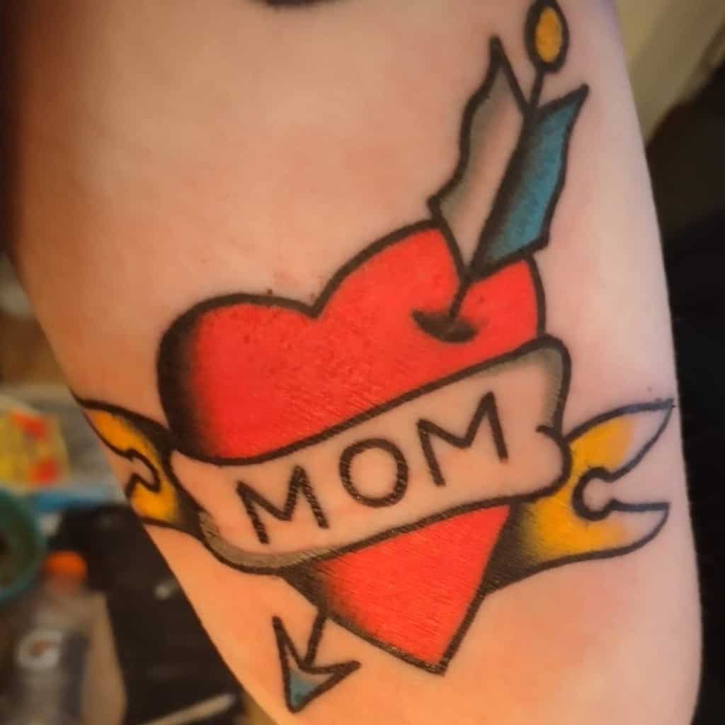 Tattoo of a heart pierced by an arrow, adorned with a banner that proudly reads "Mom"