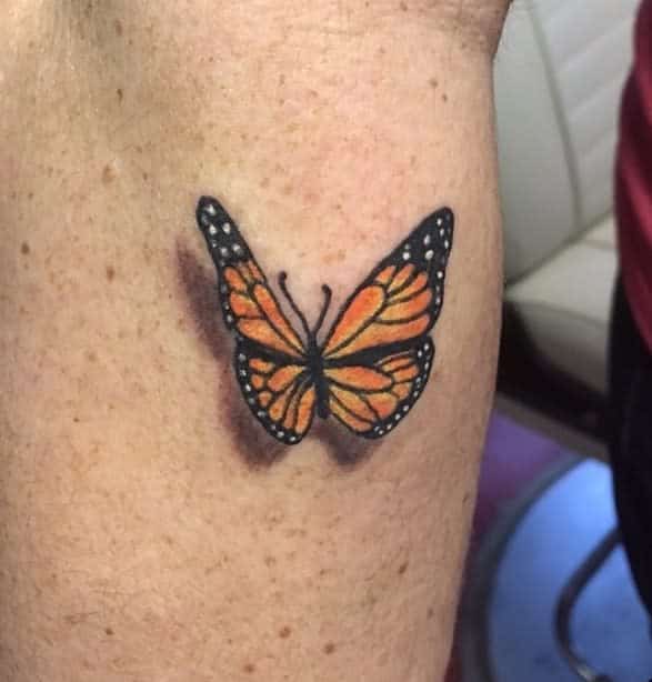 A monarch butterfly tattoo graces the skin, its vibrant orange and black wings capturing a timeless elegance