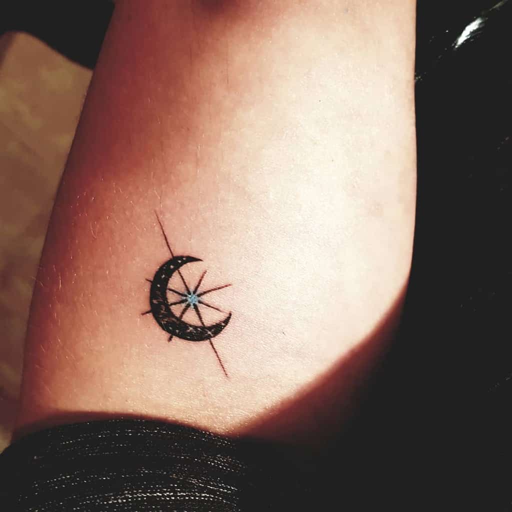 Tattoo of a crescent moon cradling multiple stars on a person's arm