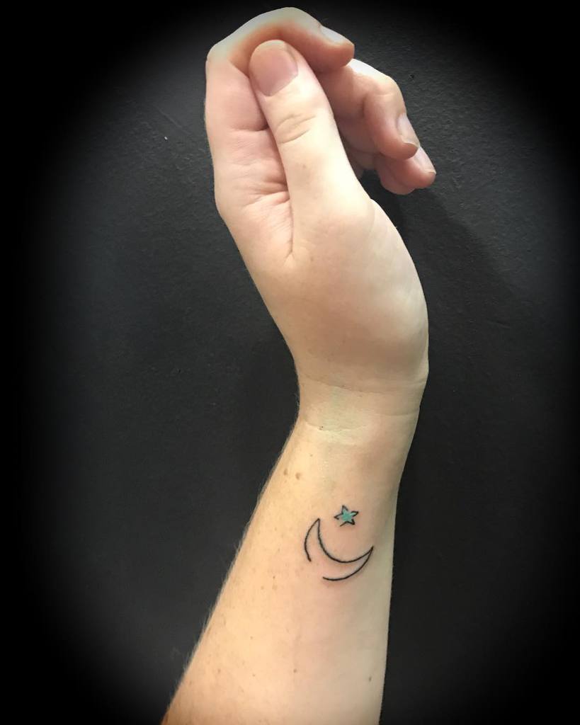 Simple star and crescent moon tattoo on the inner wrist of an upturned hand against a dark, star-speckled background