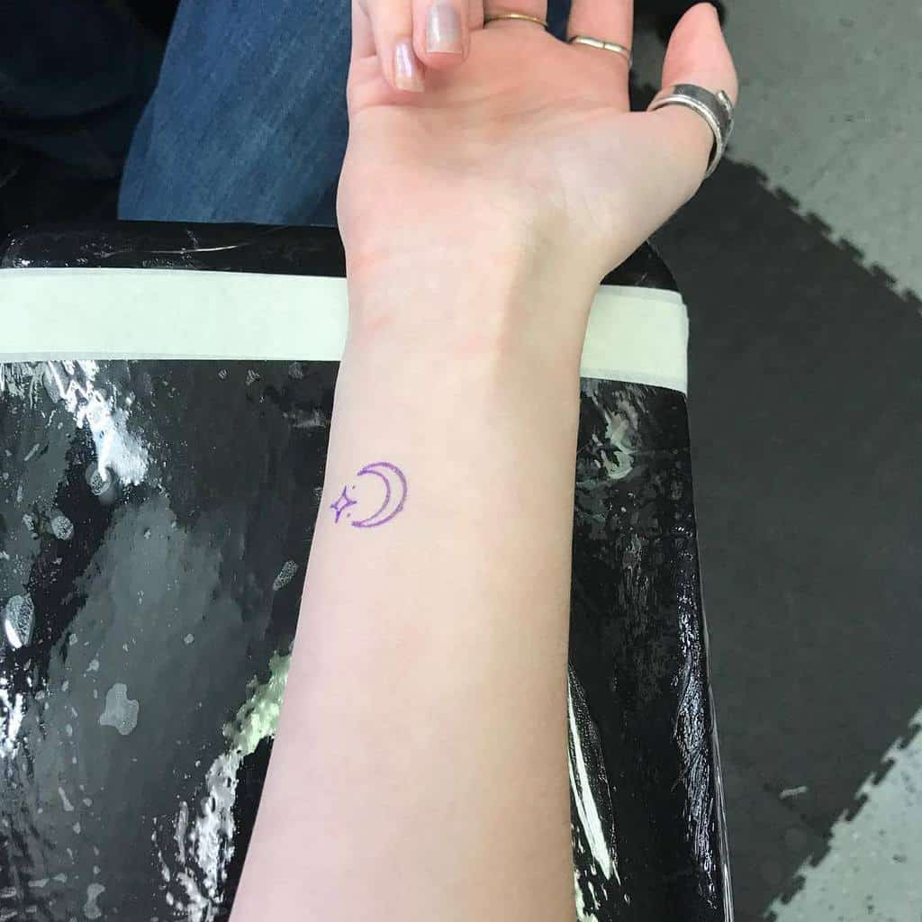 Forearm tattoo of a crescent moon adorned with stars, shown on a stretched arm