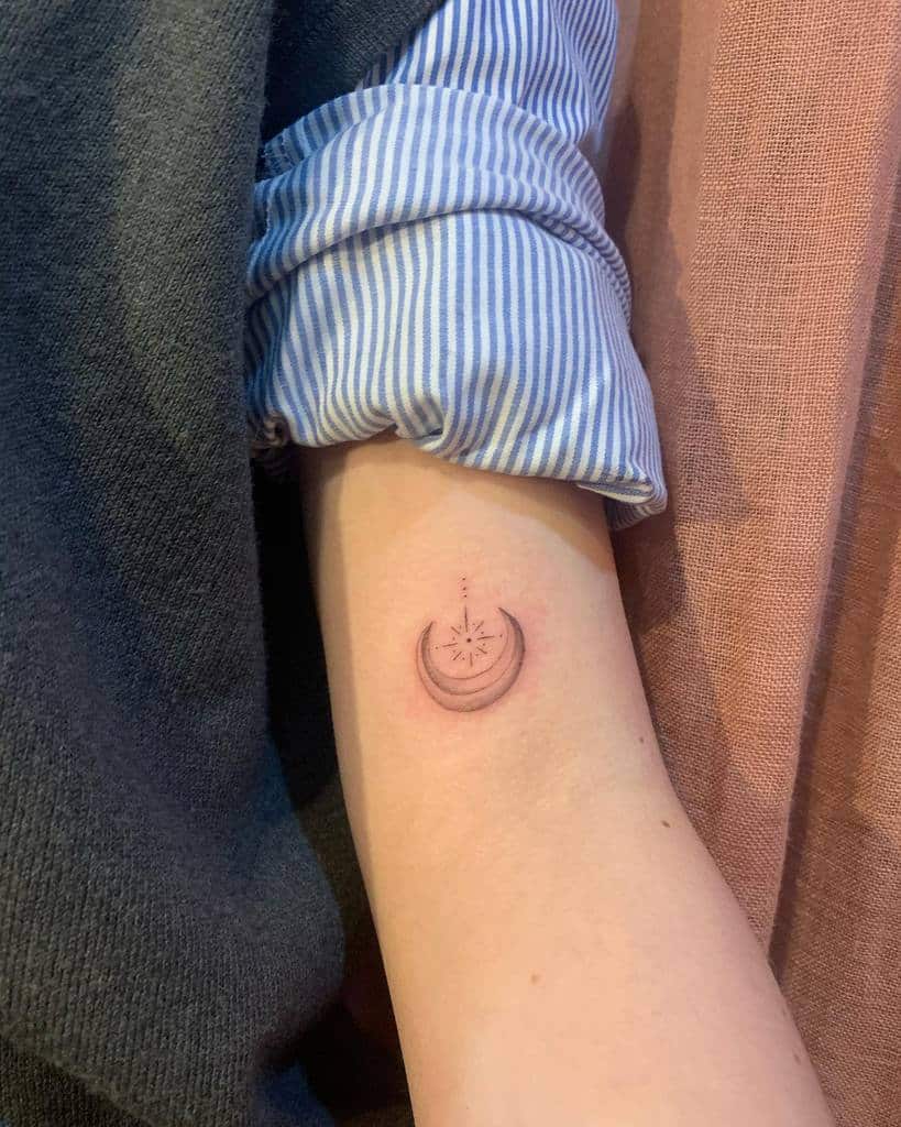 A small crescent moon tattoo on the inner arm with a delicate star at its center