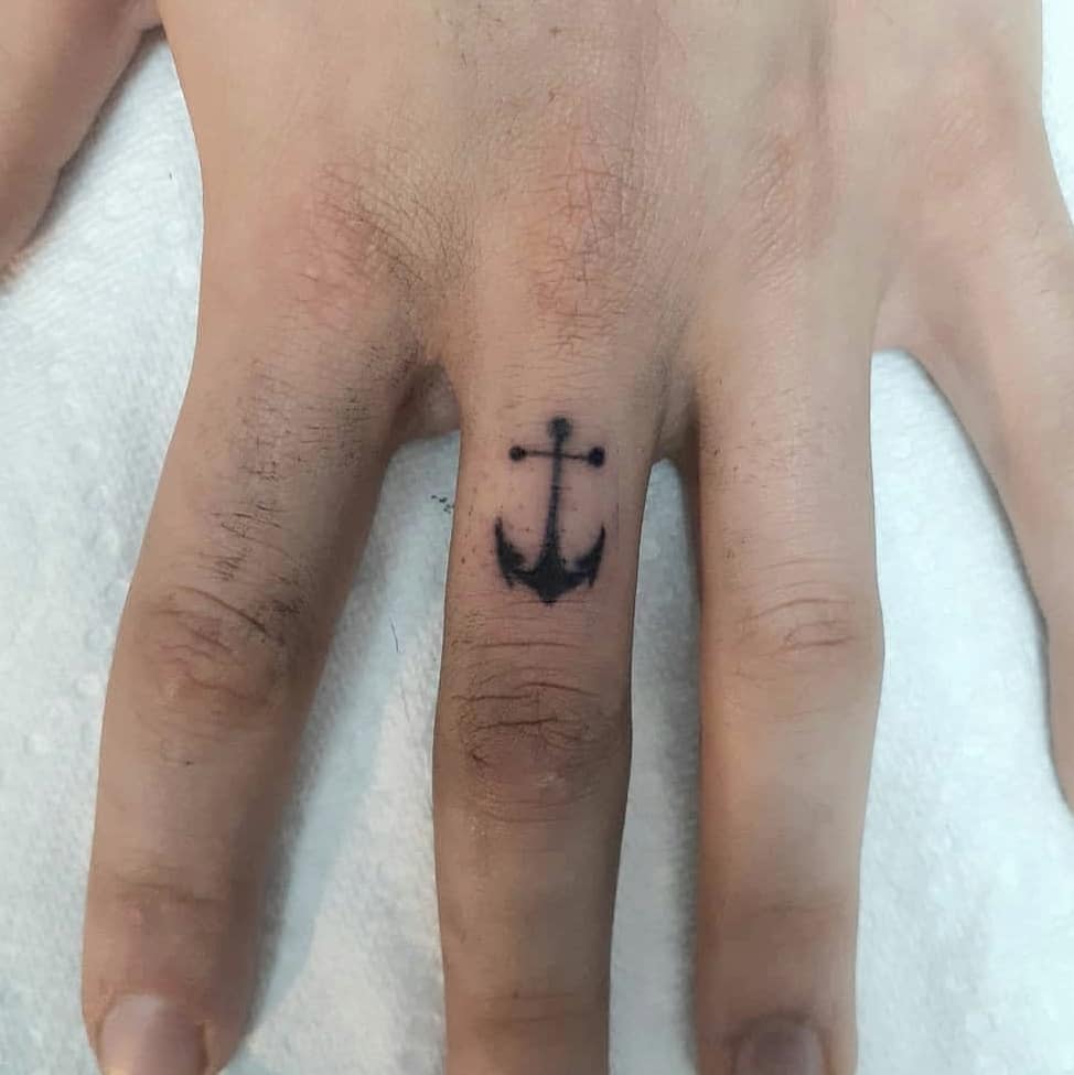 Navy anchor tattoo on the middle finger of a person's hand