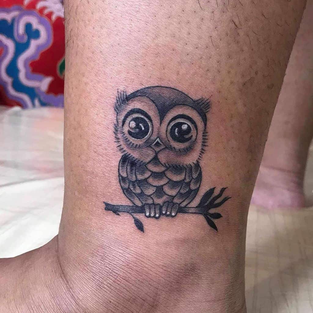A cute, detailed owl perched on a branch with large eyes, done in soft black and gray shading, creating an adorable, cartoonish style