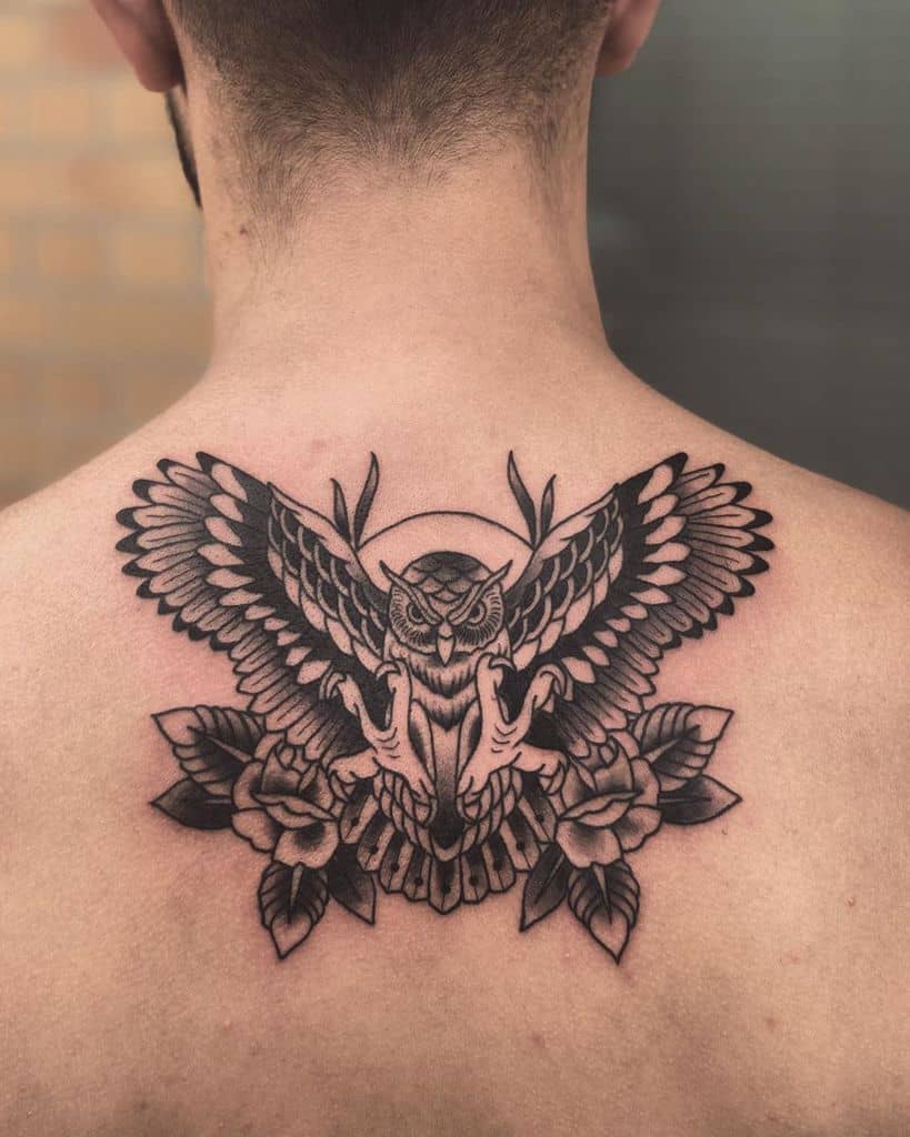 An enchanting back tattoo featuring an owl with majestic wings spread wide, gracefully encircled by delicate roses