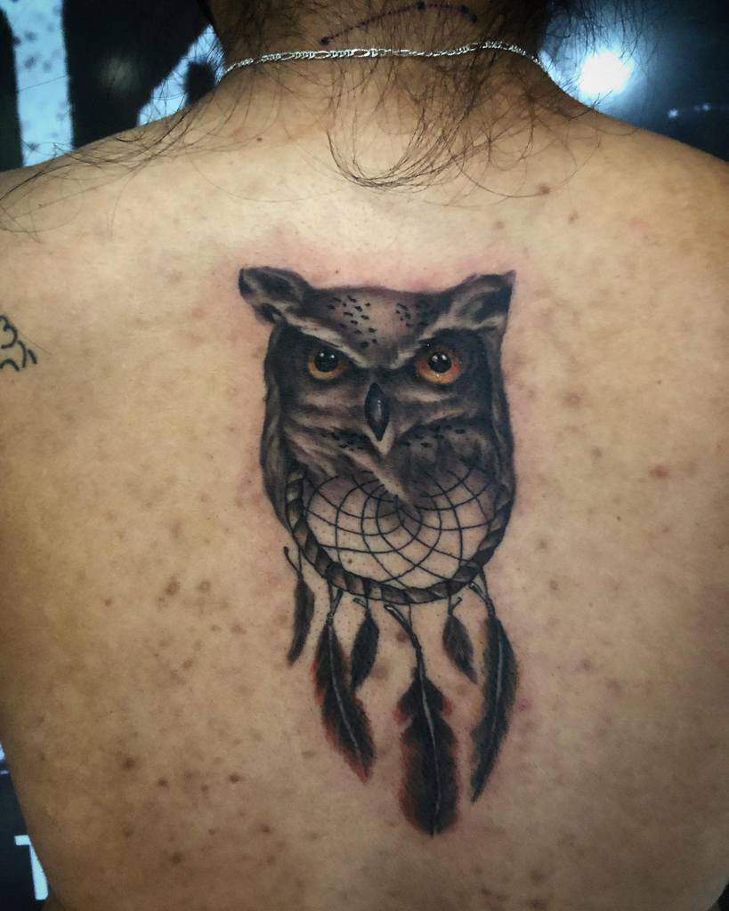 A captivating back tattoo featuring an intricately detailed owl elegantly intertwined with a dreamcatcher design