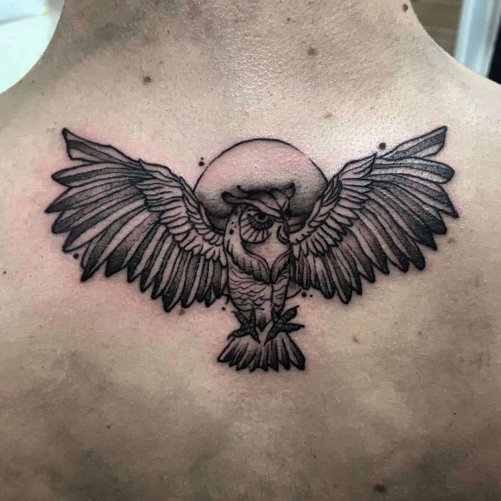 A striking tattoo of an owl with outstretched wings on the upper back, designed in bold black lines and detailed shading, with a moon in the background