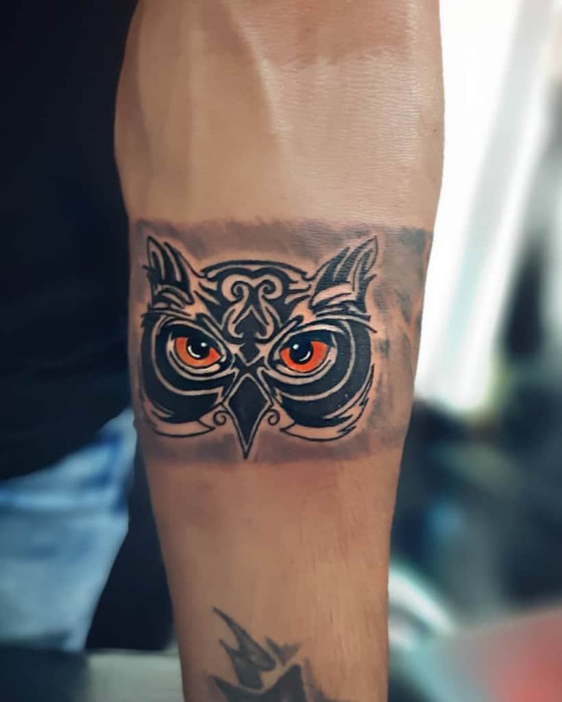 A tattoo of a stylized owl with piercing orange eyes graces a forearm