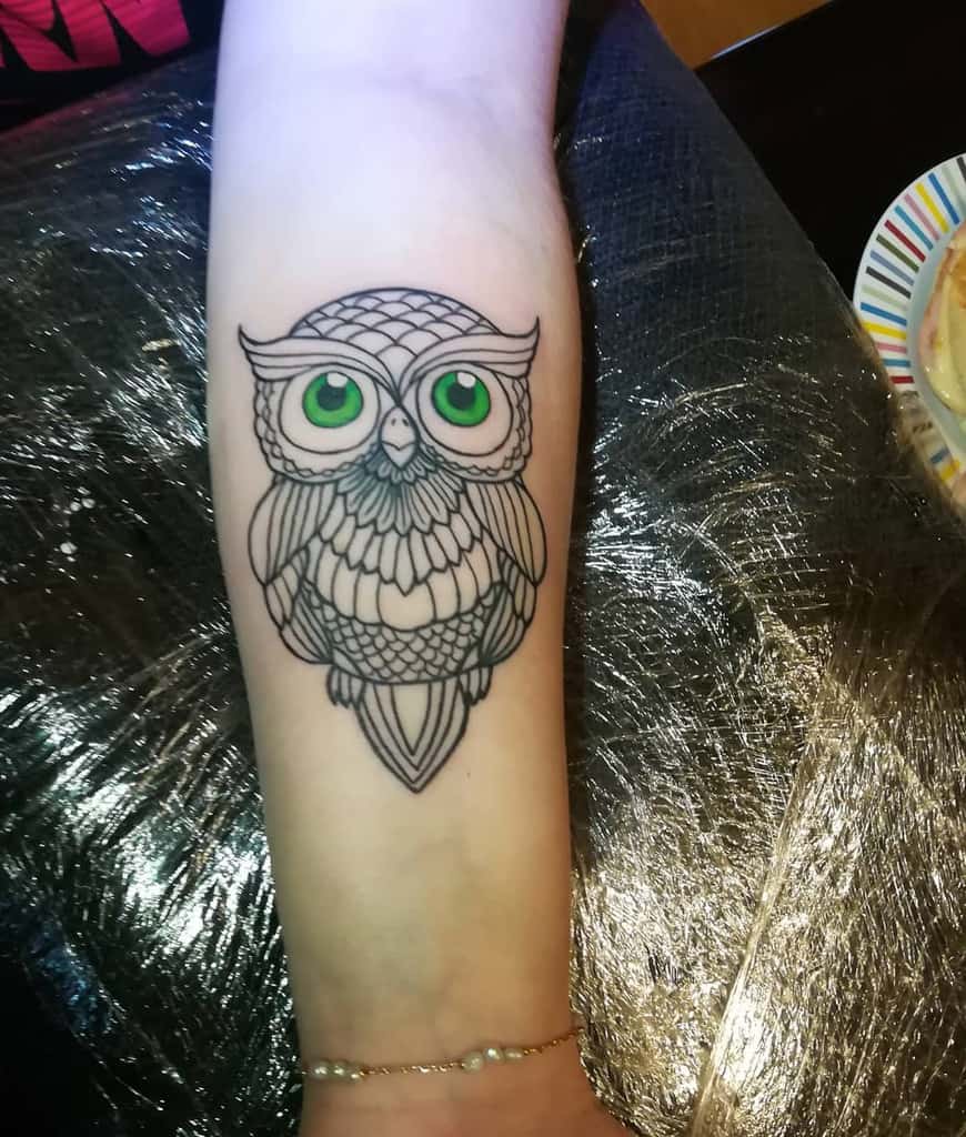 A meticulously crafted arm tattoo features a detailed owl, its piercing green eyes capturing the essence of wisdom and mystery