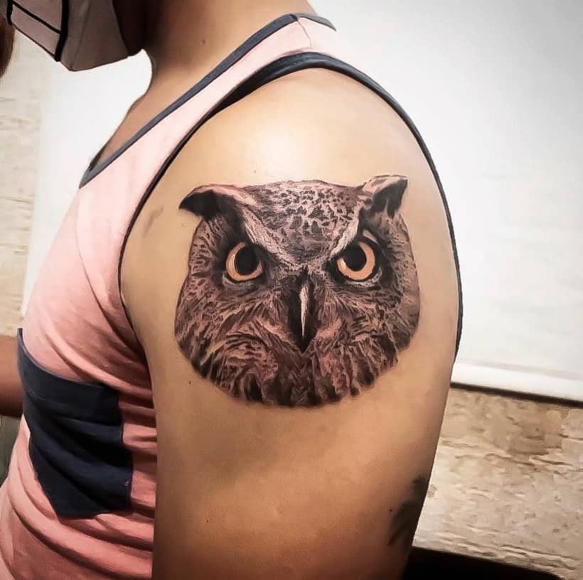 A realistic owl tattoo on the shoulder, featuring detailed feathers and intense, captivating eyes, showcasing the bird's sharp focus