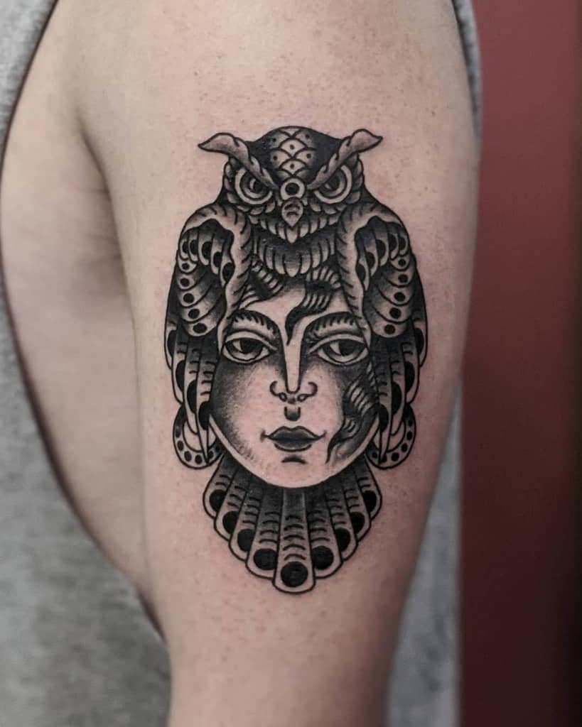 A striking tattoo features a woman's face with an owl perched above, intricately detailed in black ink on the upper arm