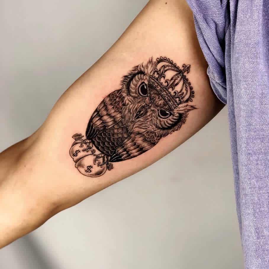 A tattoo of an owl wearing a crown next to a bag of money on a person's arm
