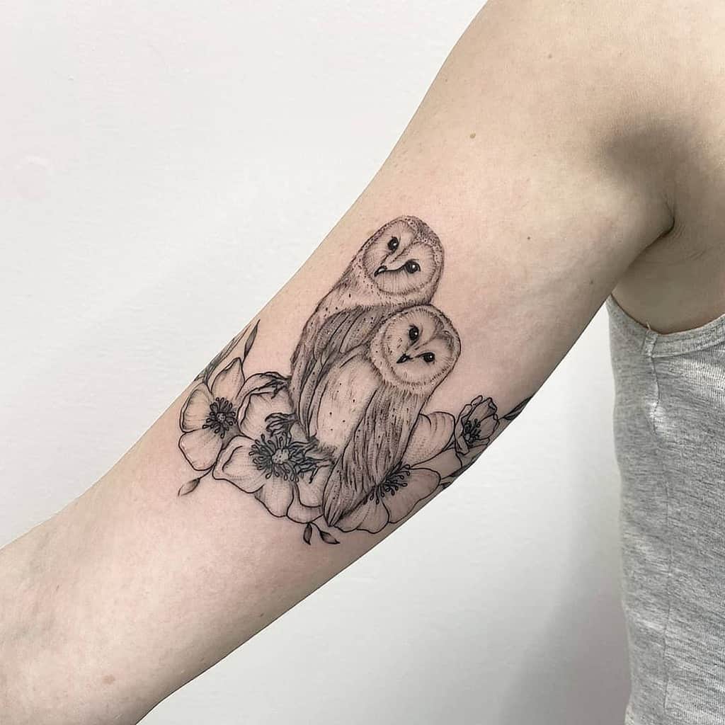 Tattoo of two owls perched on flowers on an upper arm