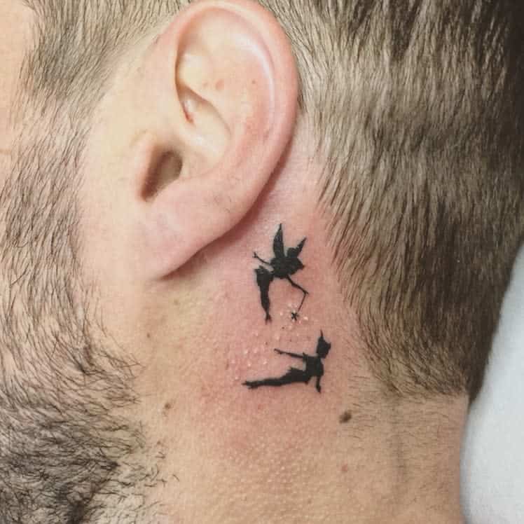 Small black ink tattoo of Peter Pan flying towards Tinker Bell, who sprinkles pixie dust