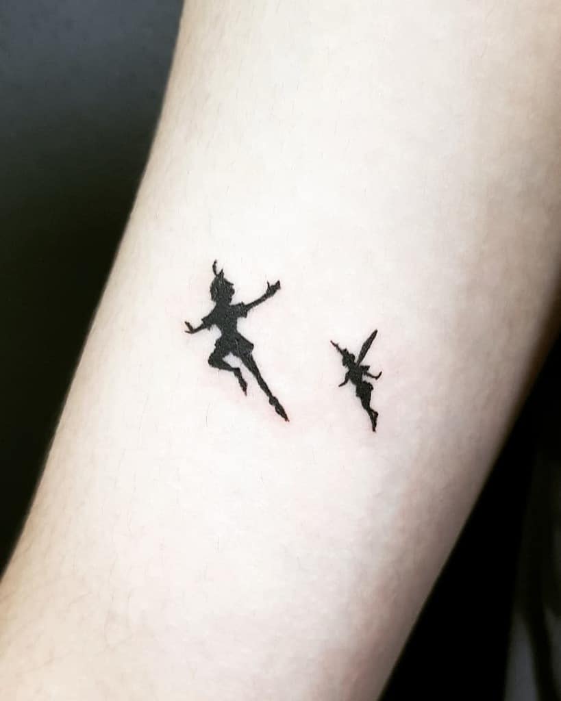 Minimalist black ink tattoo of Peter Pan and Tinker Bell flying, symbolizing magic and adventure
